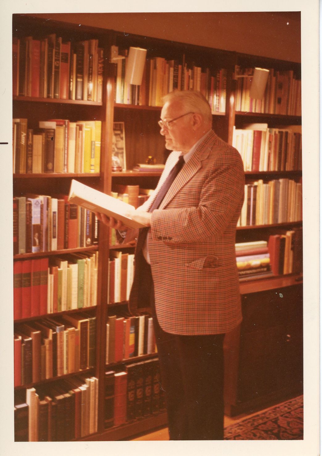 John Howard Birss standing with book in hand in front of bookshelves.